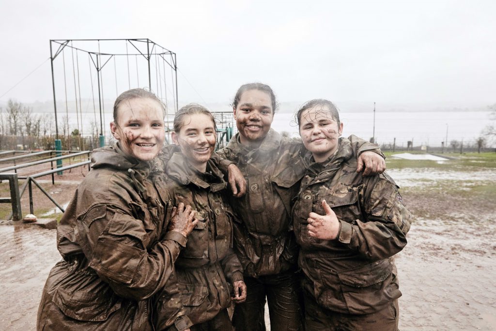 A group of female Royal Marines cadets smile for the camera with mud on their faces