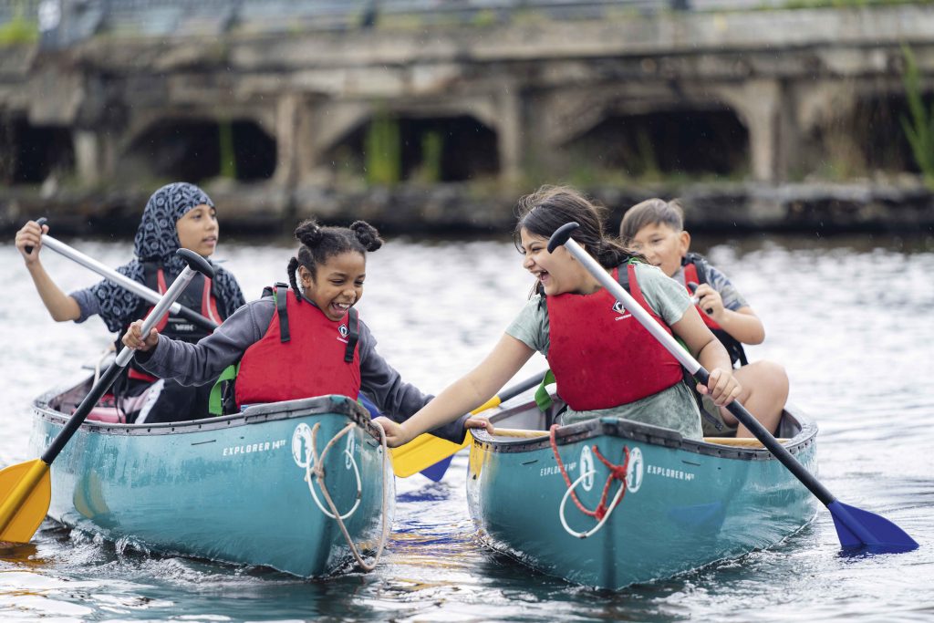 young people of different ethnic backgrounds in canoes, rowing and smiling