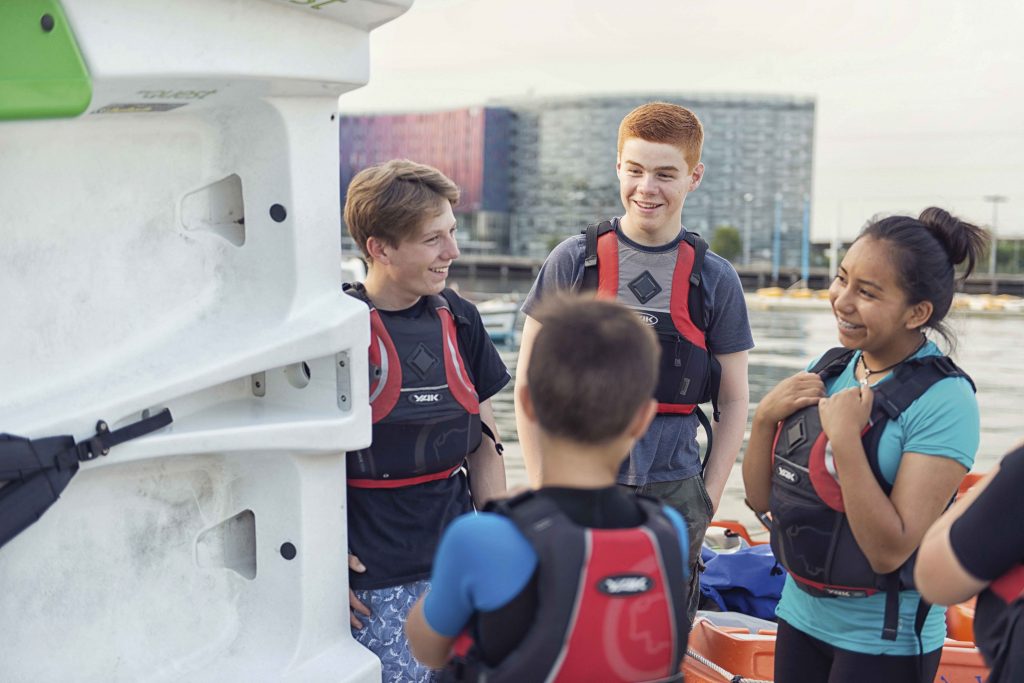 A group of cadets wearing life jackets chat and smile together as they get ready to out on the water