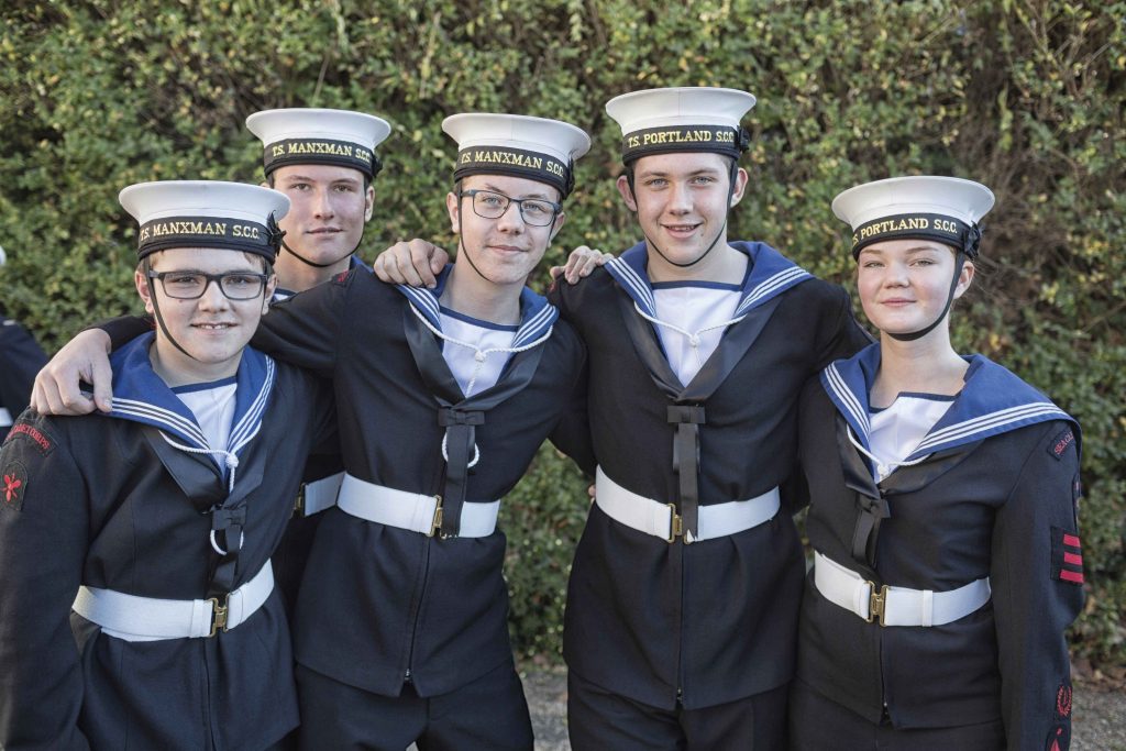 A group of sea cadets in uniform with their arms around each others shoulders smile at the camera on Trafalgar Day