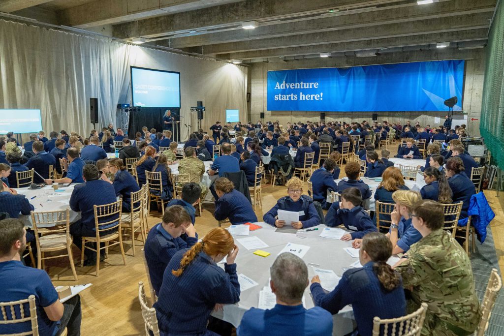 A big room with cadets sitting around tables working together 