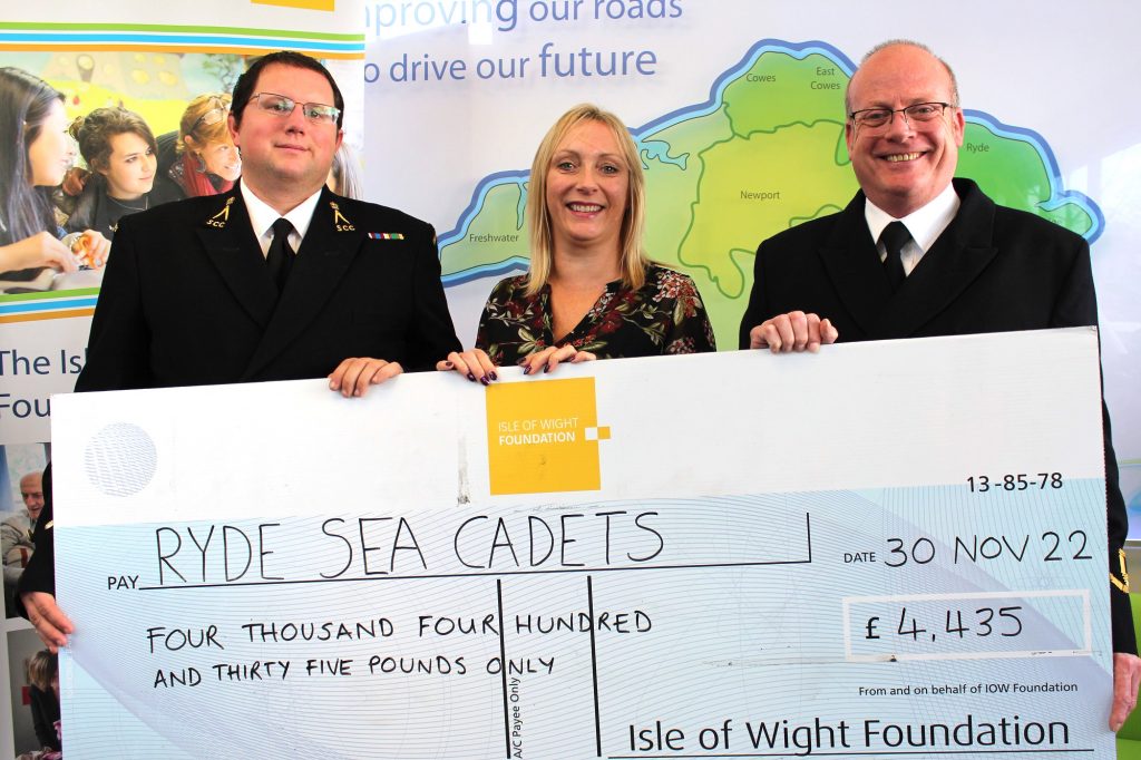 Three adults hold up a giant check made out to sea cadets