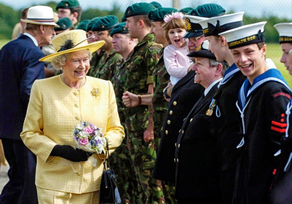 HM The Queen in a yellow dress and hat talking and smiling with sea cadets