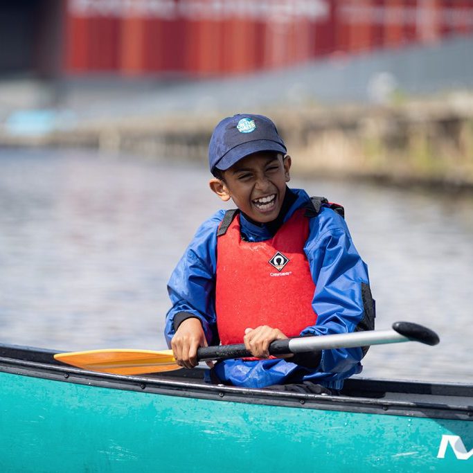 Photo of a young person smiling and holding an oar in a boat