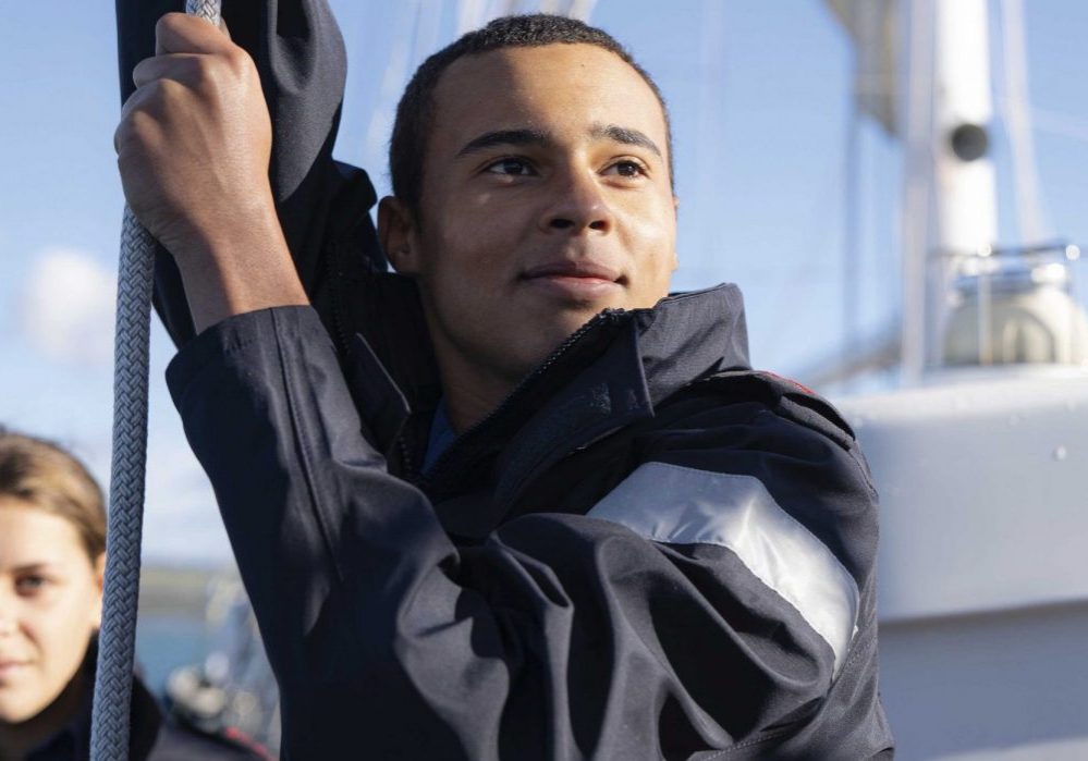 a black cadet smiles off camera as he hoists the sails on board TS Royalist